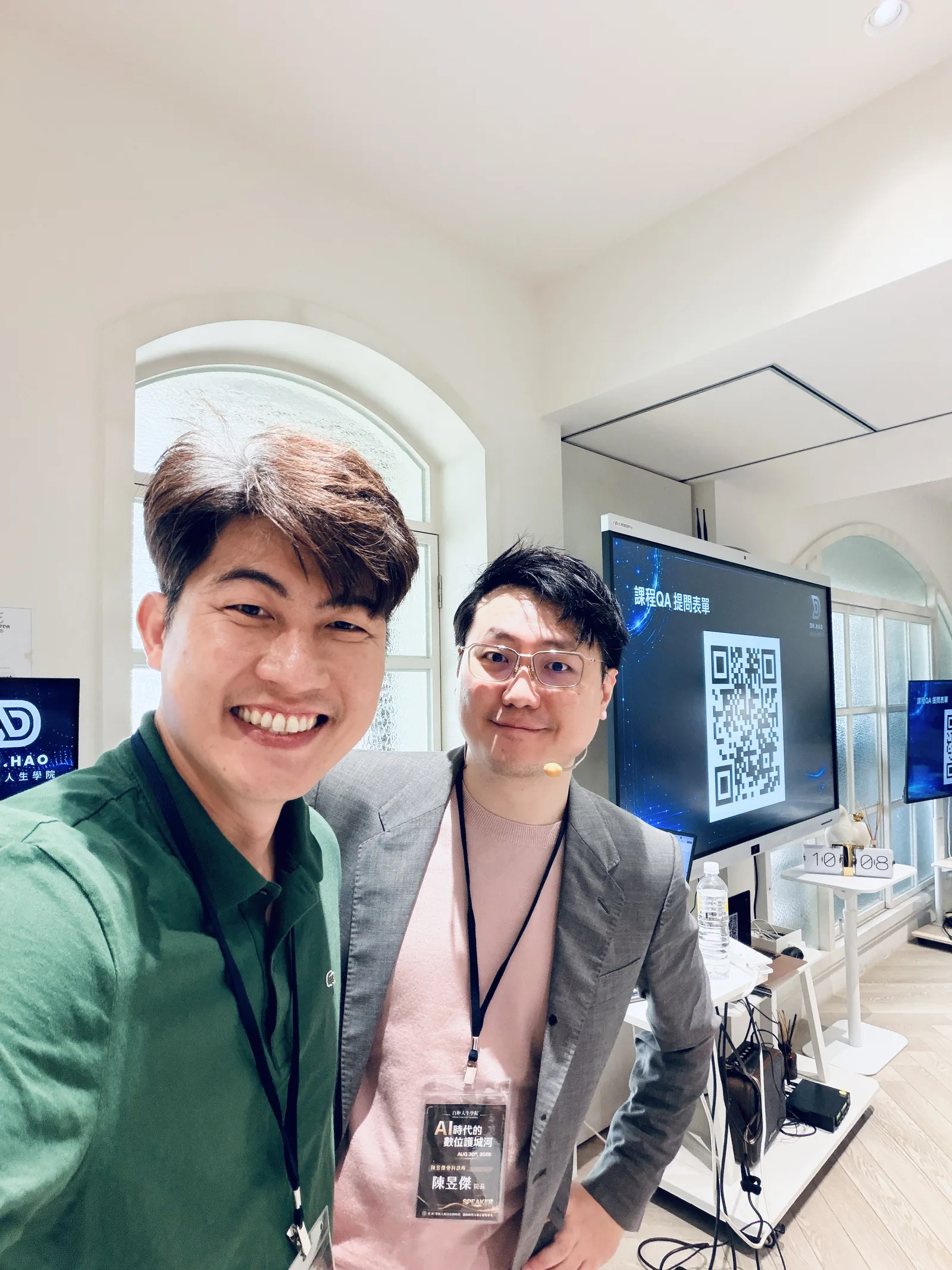 張益豪醫師與掛著 SPEAKER 講師證的陳昱傑醫師在課程現場合影，背景螢幕是課程問答表單的 QR code