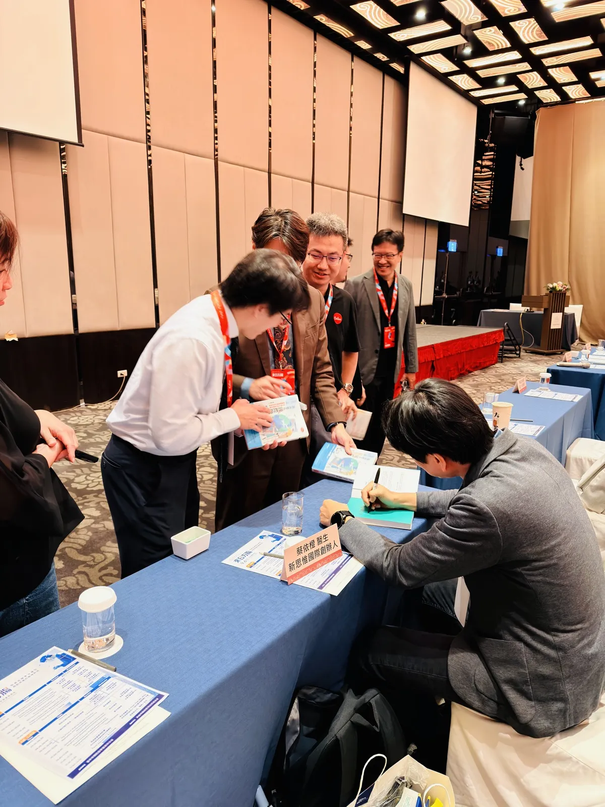 蔡依橙醫師低頭在書上簽名，桌牌寫著「蔡依橙醫生 新思惟國際創辦人」