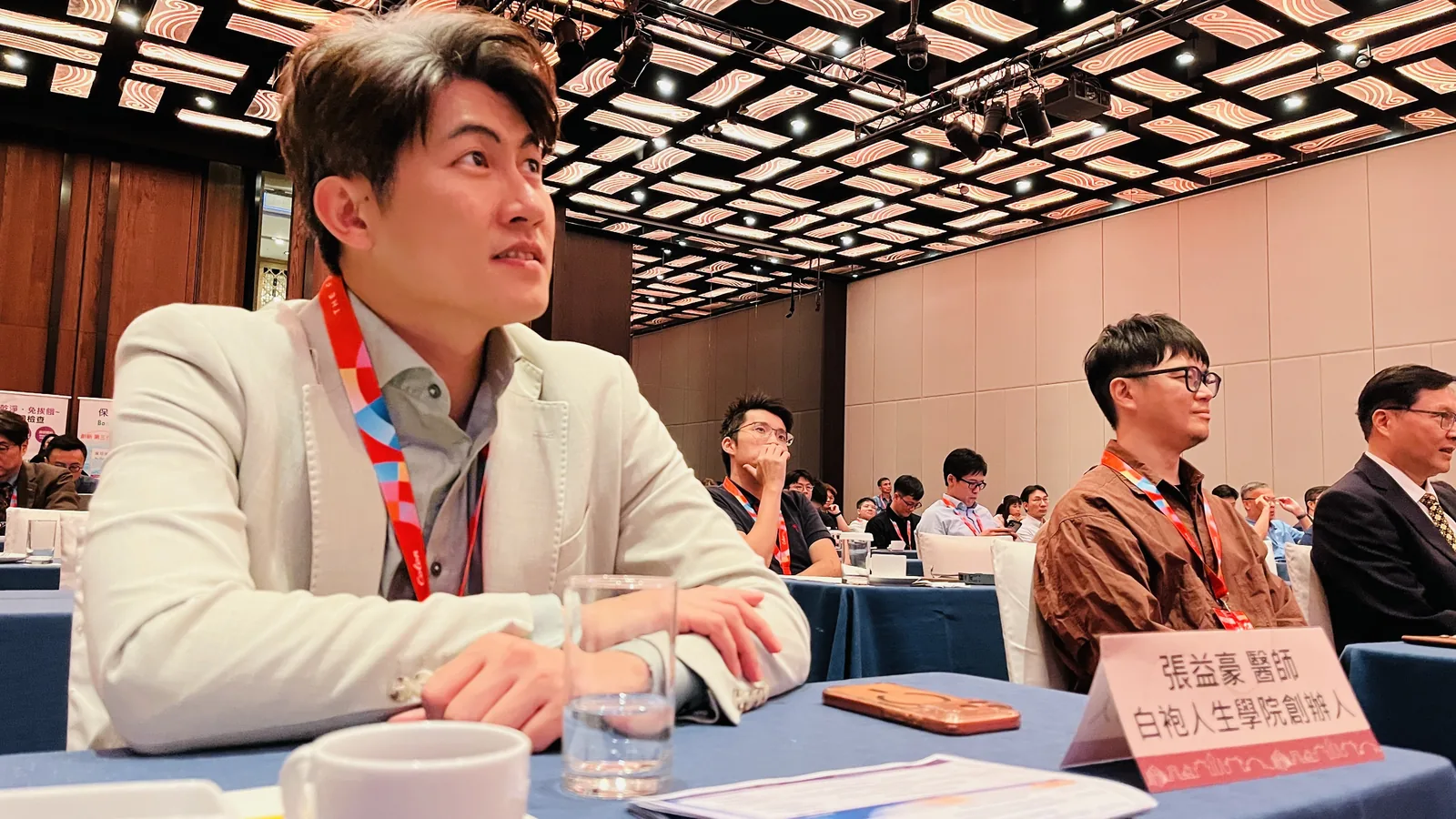 張益豪醫師坐在來日方腸 2026 研討會台下聽講，桌牌寫著張益豪醫師、白袍人生學院創辦人