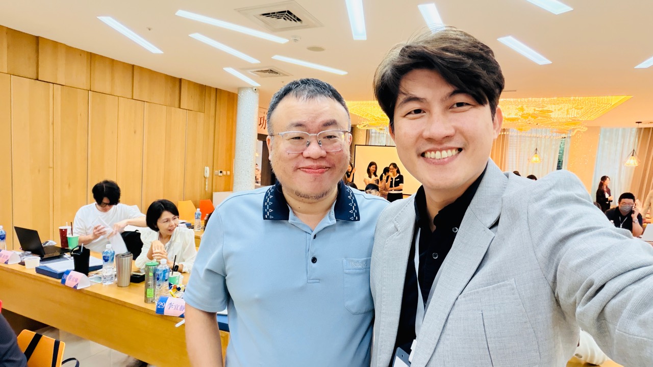 兩位參與者在課程教室內合影，背景可見課桌與其他參與者。