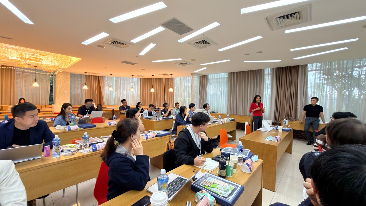 一位學員在座位旁持麥克風發言，講者與其他學員聆聽。