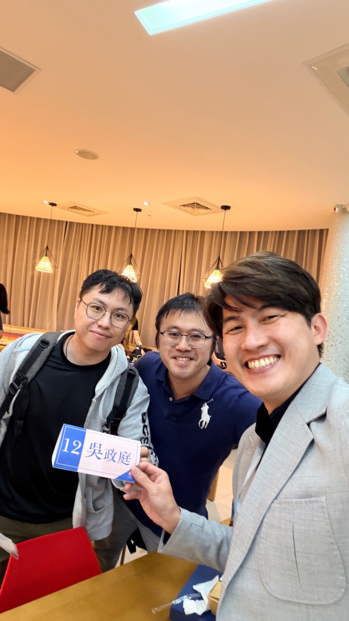 三位參與者在座位旁合影，其中一人拿著桌牌。