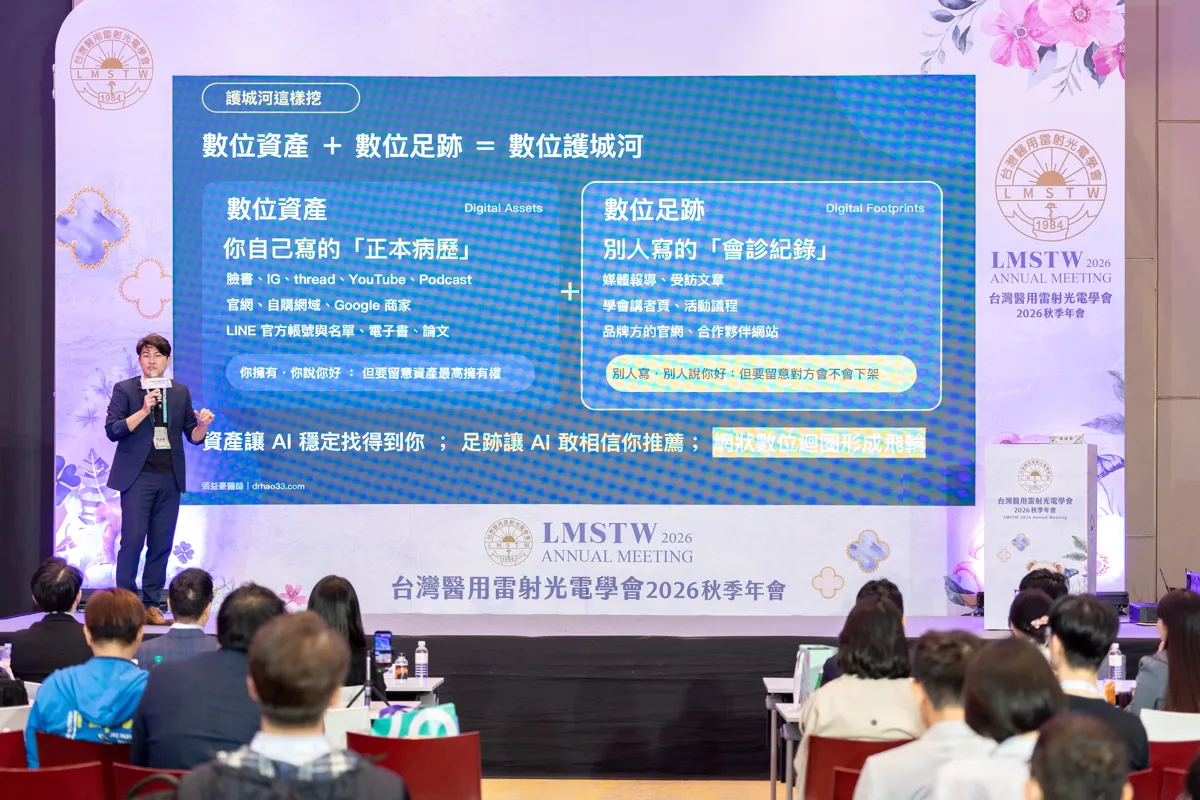 張益豪醫師在舞台左側，身後螢幕顯示「數位資產＋數位足跡＝數位護城河」投影片，台前坐滿聽眾