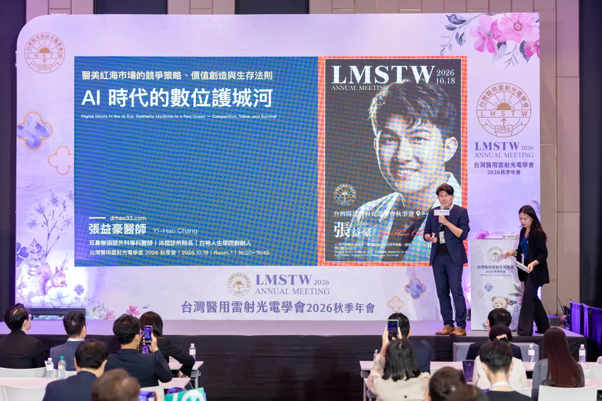 張益豪醫師站在台灣醫用雷射光電學會 2026 秋季年會 ROOM 1 舞台上，身後大螢幕顯示講題「AI 時代的數位護城河」