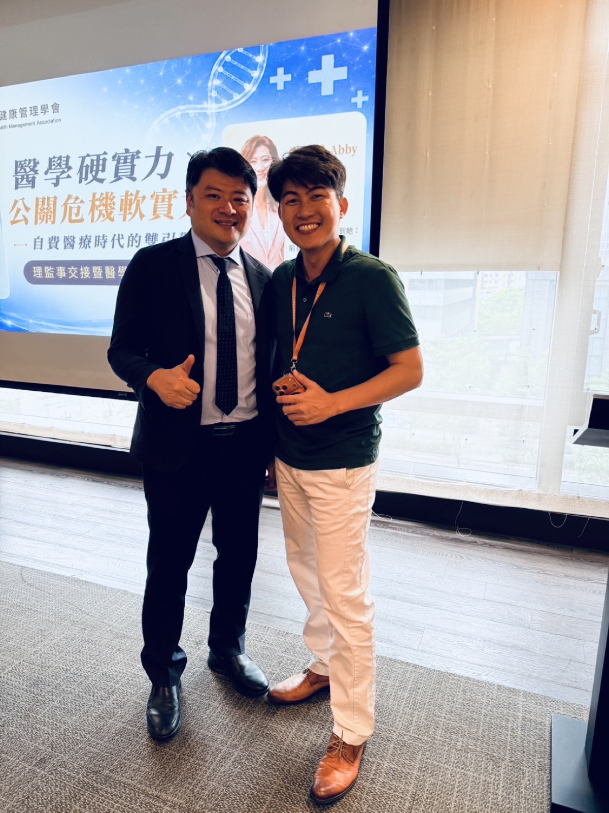 張益豪醫師與王舒民醫師在研討會講題背板前合影，背板顯示醫學硬實力與公關危機軟實力主題與講者謝馨慧Abby的介紹，王舒民醫師比出大拇指