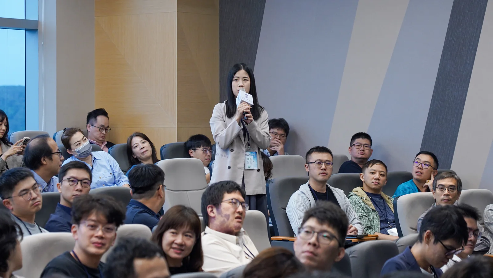 2026 年會一位參與者在座位區起身持麥克風發問，其他與會者聆聽