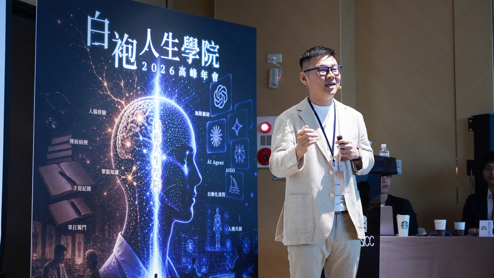 2026 高峰年會講者手持簡報器分享，身旁為從人腦到 AI 腦的活動背板