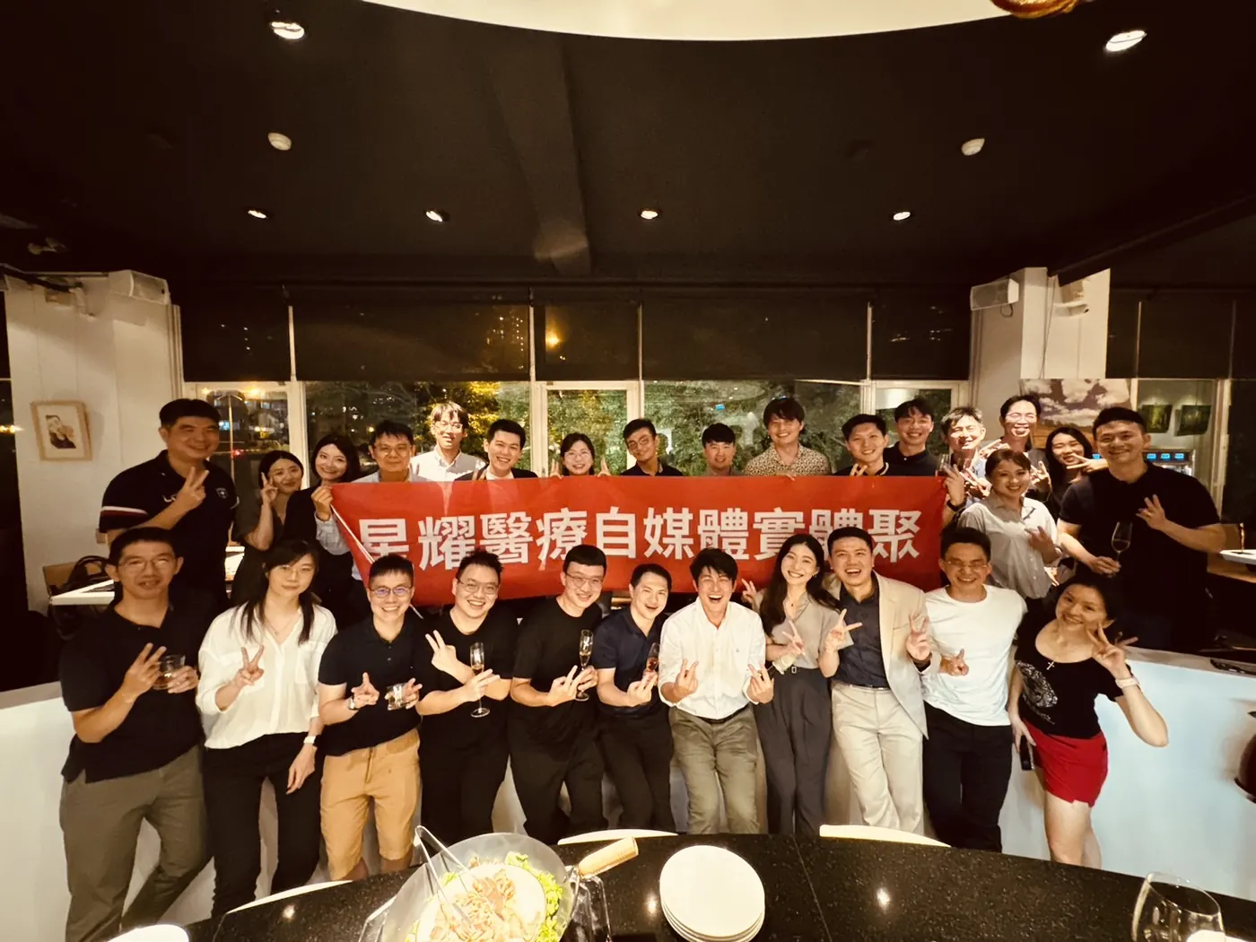 與會者在 Bistro 302 吧台前拉起紅色「星耀醫療自媒體實體聚」布條大合照，比著手勢