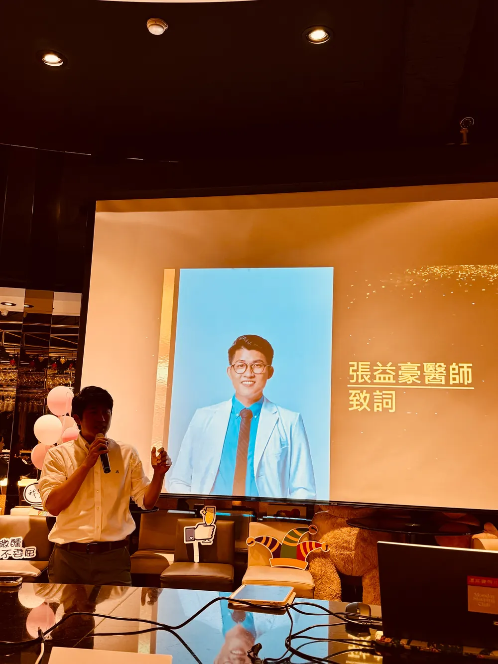 投影幕上是張益豪醫師的白袍形象照與「張益豪醫師致詞」字樣，前方有人手持麥克風