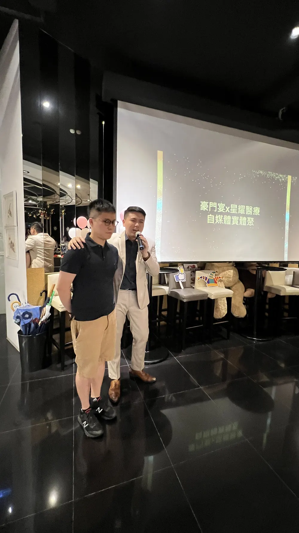 兩位與會者站在投影幕前，其中一位手持麥克風