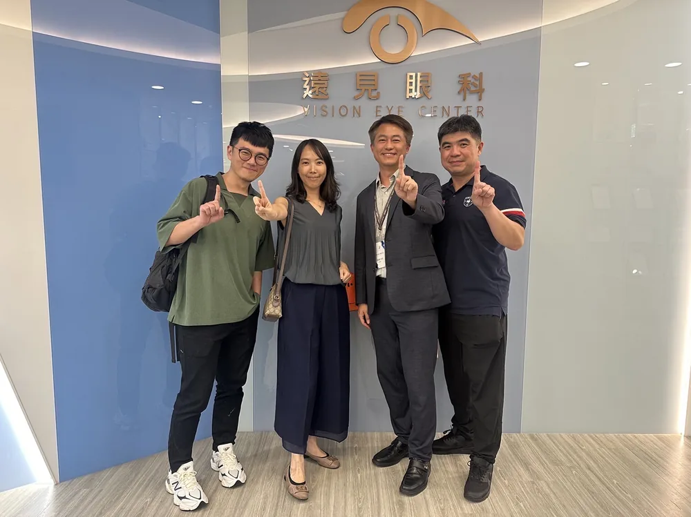 四位與會者在遠見眼科招牌前合影，一起比出「一」的手勢