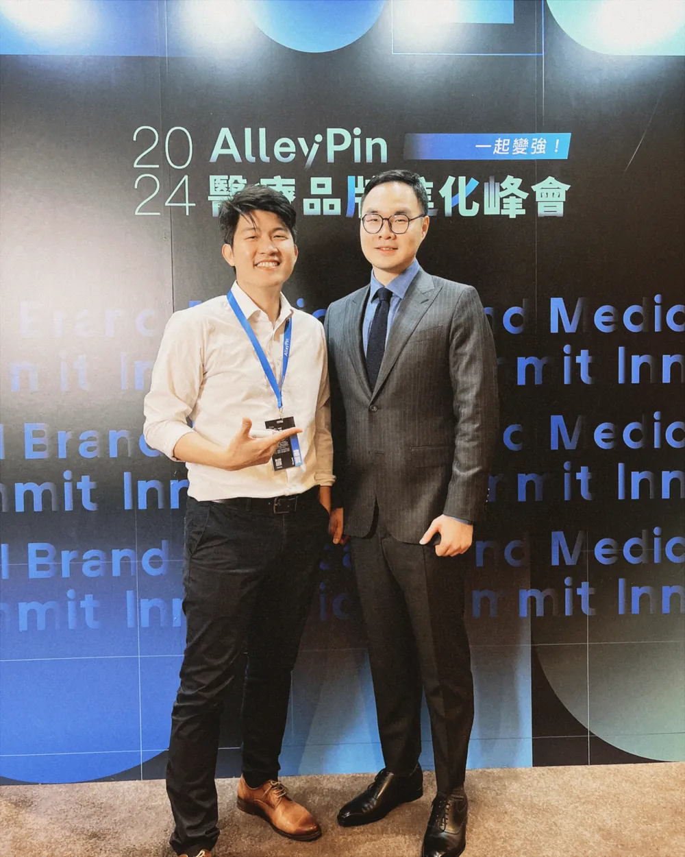 張益豪醫師與一位穿深色西裝的與會者並肩站在峰會主視覺背板前合影