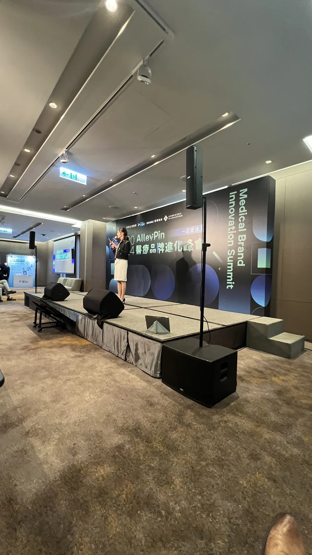 直式拍攝的舞台與音響設備，後方背板是「AlleyPin 醫療品牌進化峰會」主視覺