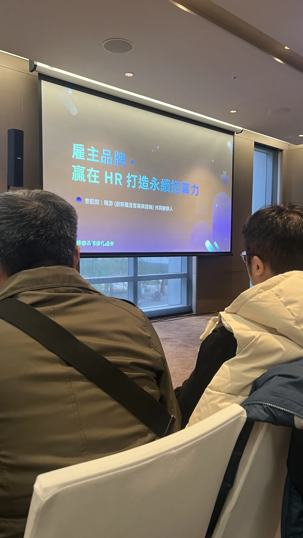 聽講視角：投影幕上的標題頁寫著「雇主品牌・贏在 HR 打造永續招募力」，前景是兩位聽眾的背影