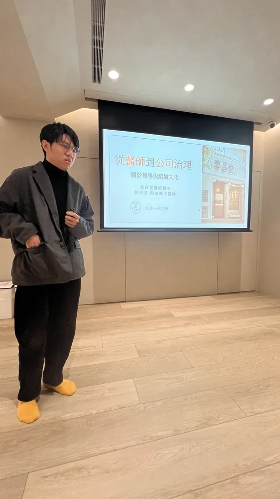 湯家誠醫師站在「從醫師到公司治理：關於領導與組織文化」標題投影片旁