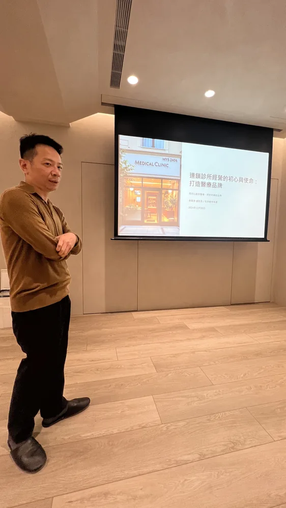 姜國彥醫師站在「連鎖診所經營的初心與使命：打造醫療品牌」標題投影片旁