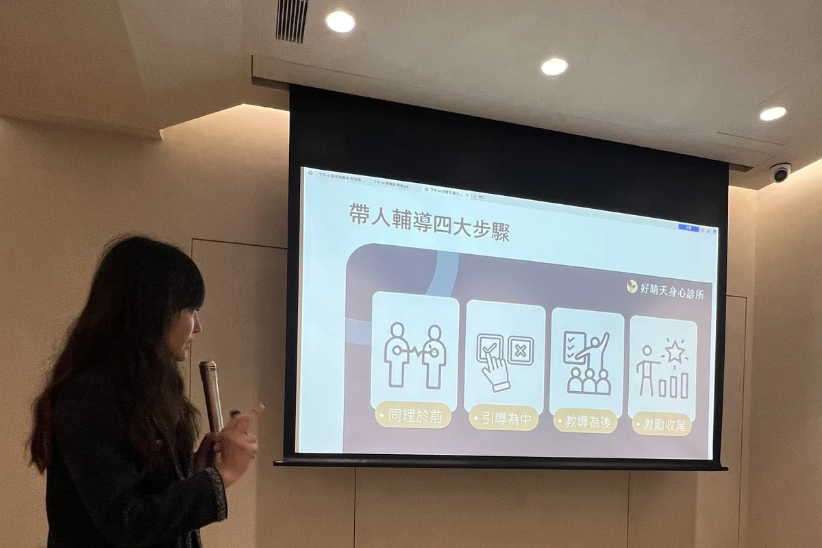 鄭晴醫師手持麥克風站在「帶人輔導四大步驟」投影片旁分享