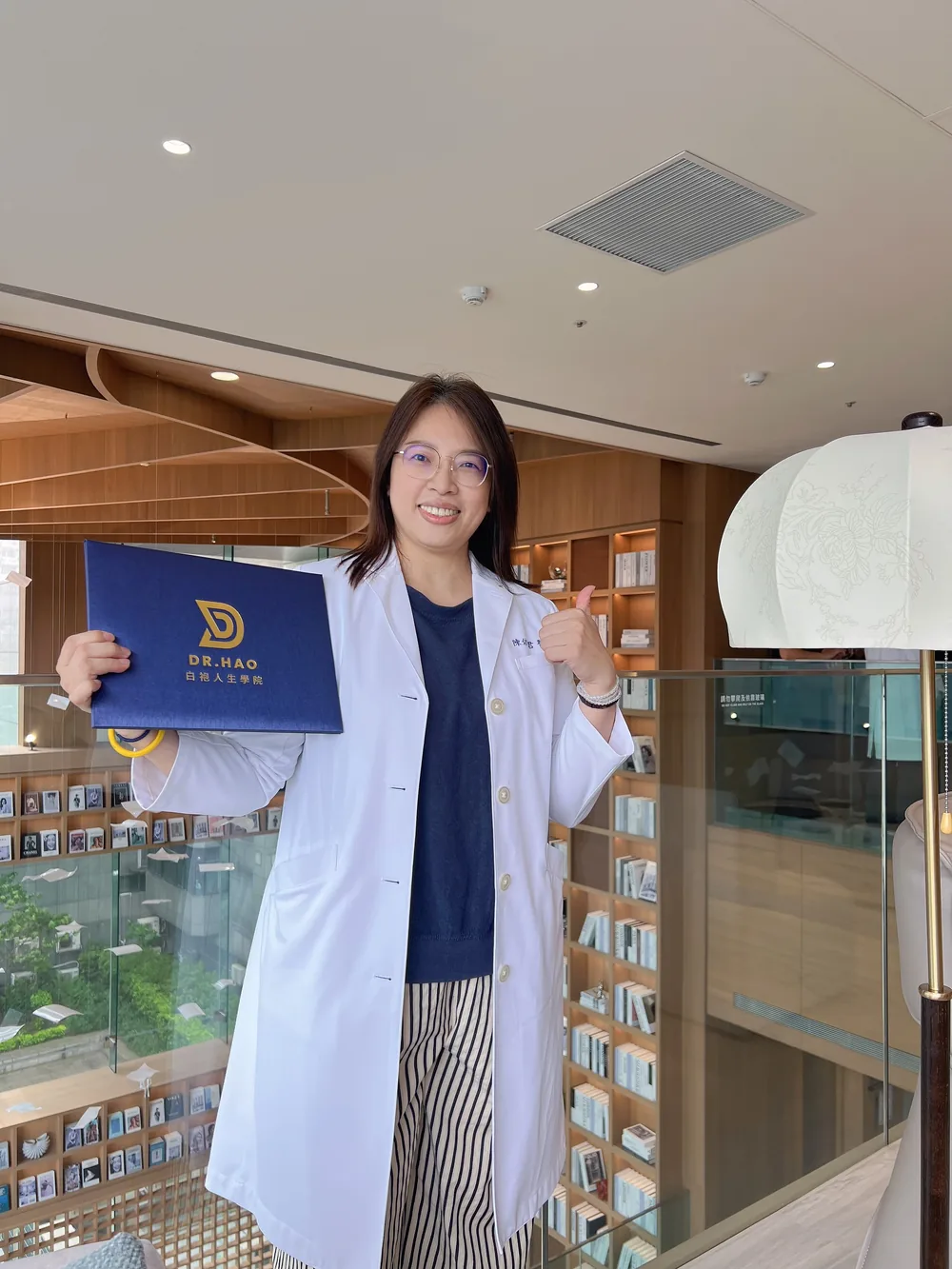 一位女醫師手持證書在書牆前合影