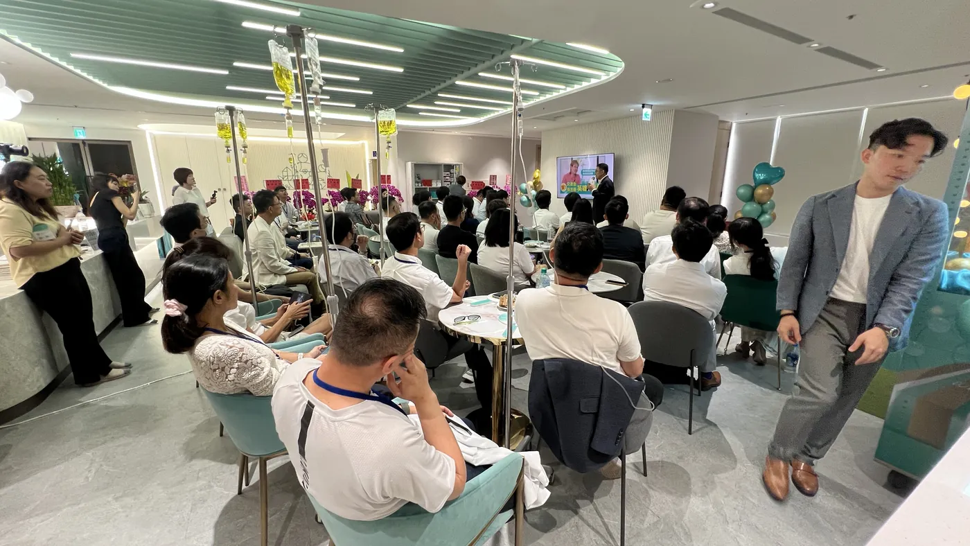 大廳坐滿與會醫師，一位穿灰色西裝外套的人站在走道上