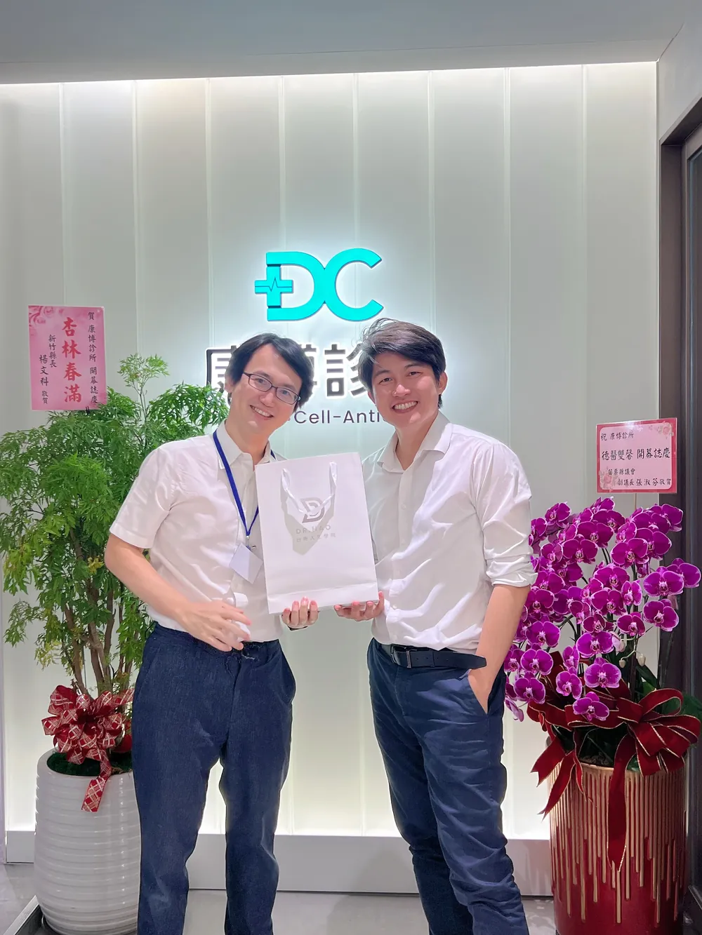張益豪醫師與謝東穎醫師在康博診所發光招牌前，一起拿著白色伴手禮袋