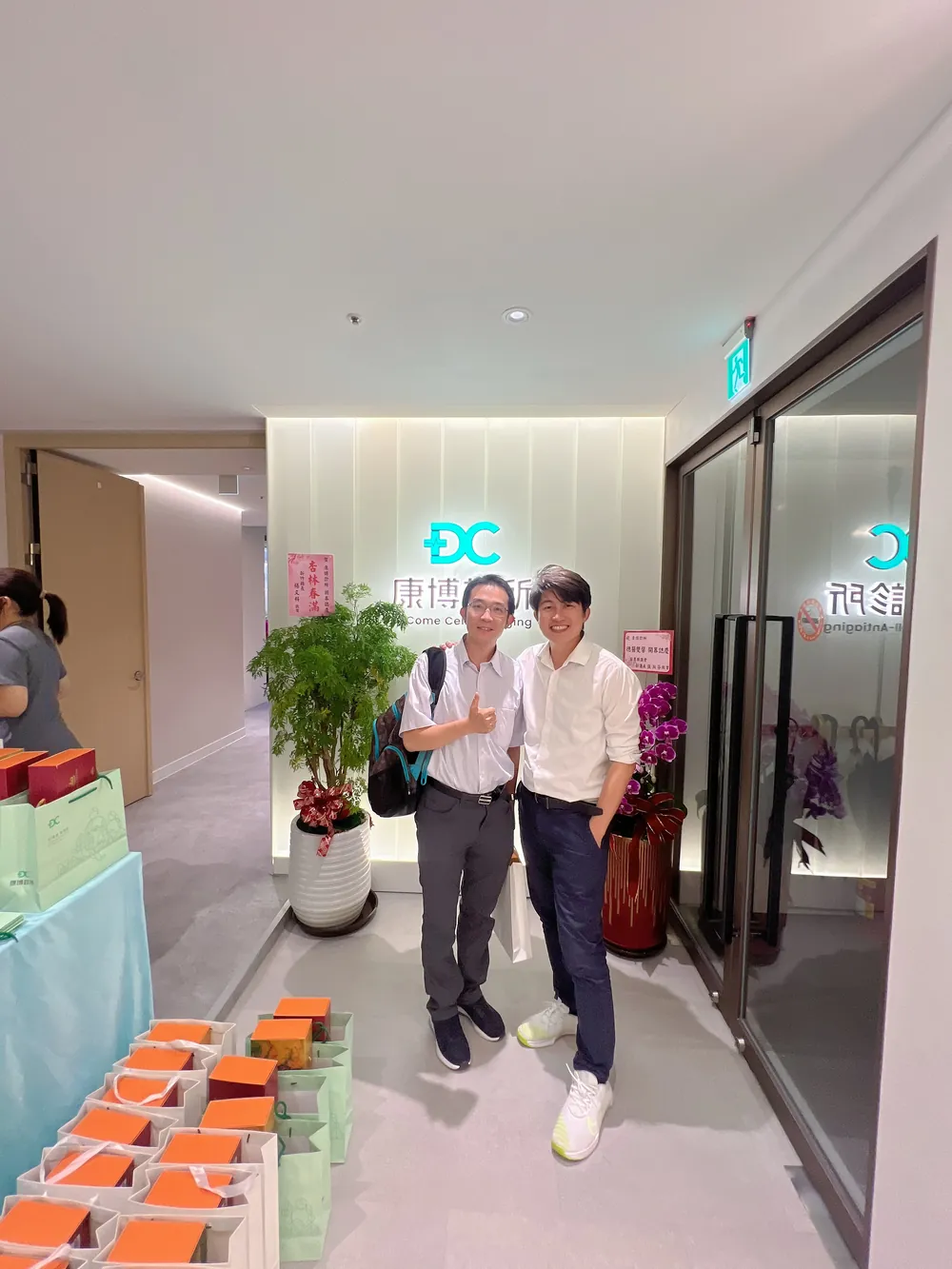 張益豪醫師與一位背著背包的醫師在招牌前合影