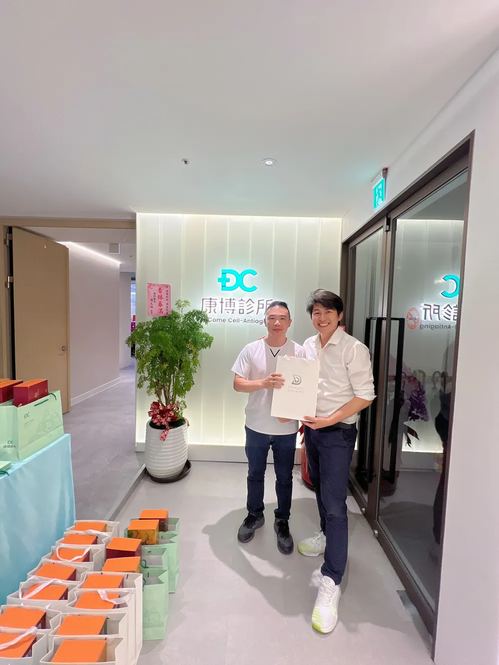 張益豪醫師與一位醫師在招牌前合影，兩人一起拿著伴手禮袋