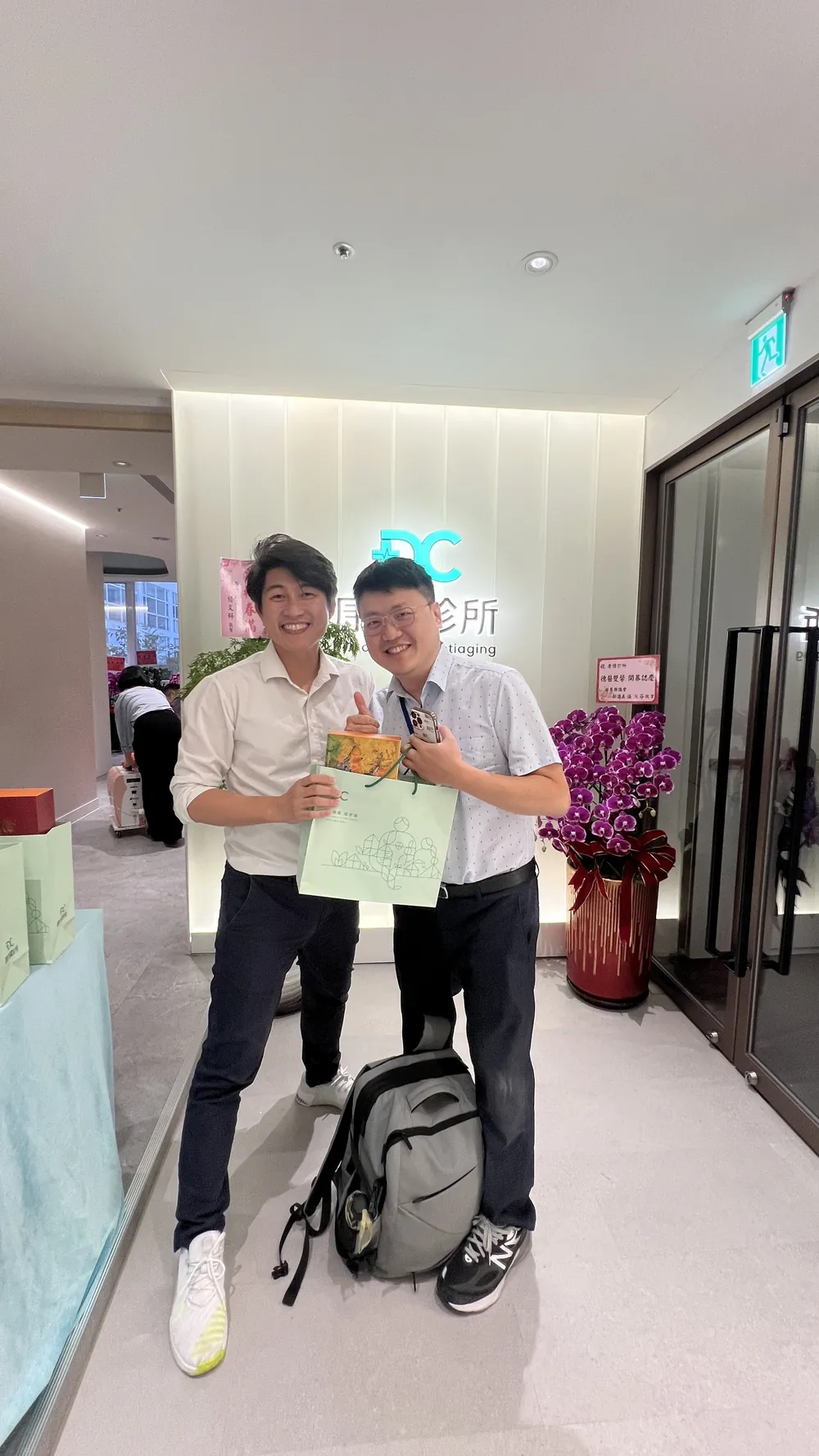 陳昱傑醫師與張益豪醫師在招牌前合影，兩人手上拿著伴手禮