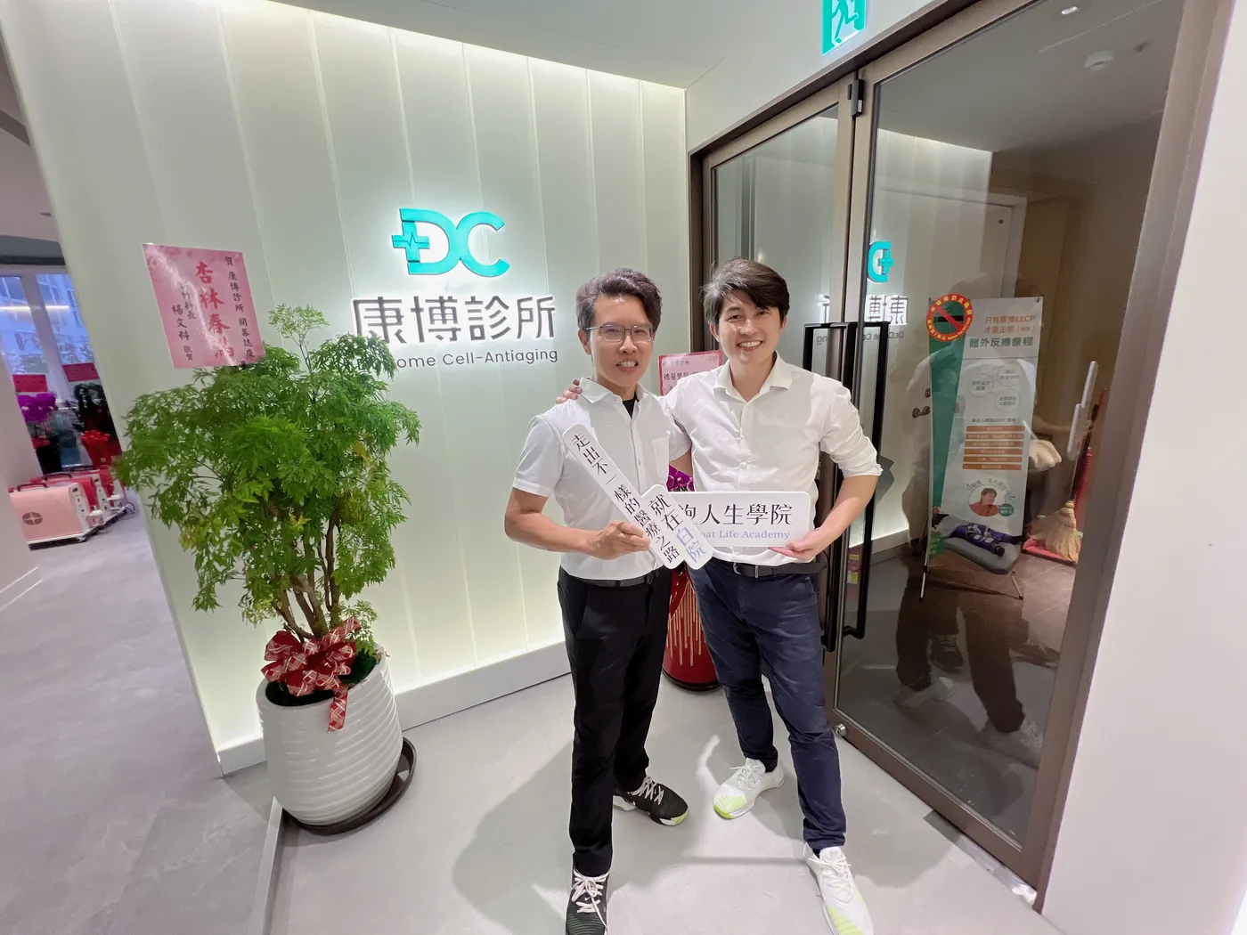 張益豪醫師與一位醫師在招牌前，一起舉著「白袍人生學院」與「走出不一樣的醫療之路」立牌