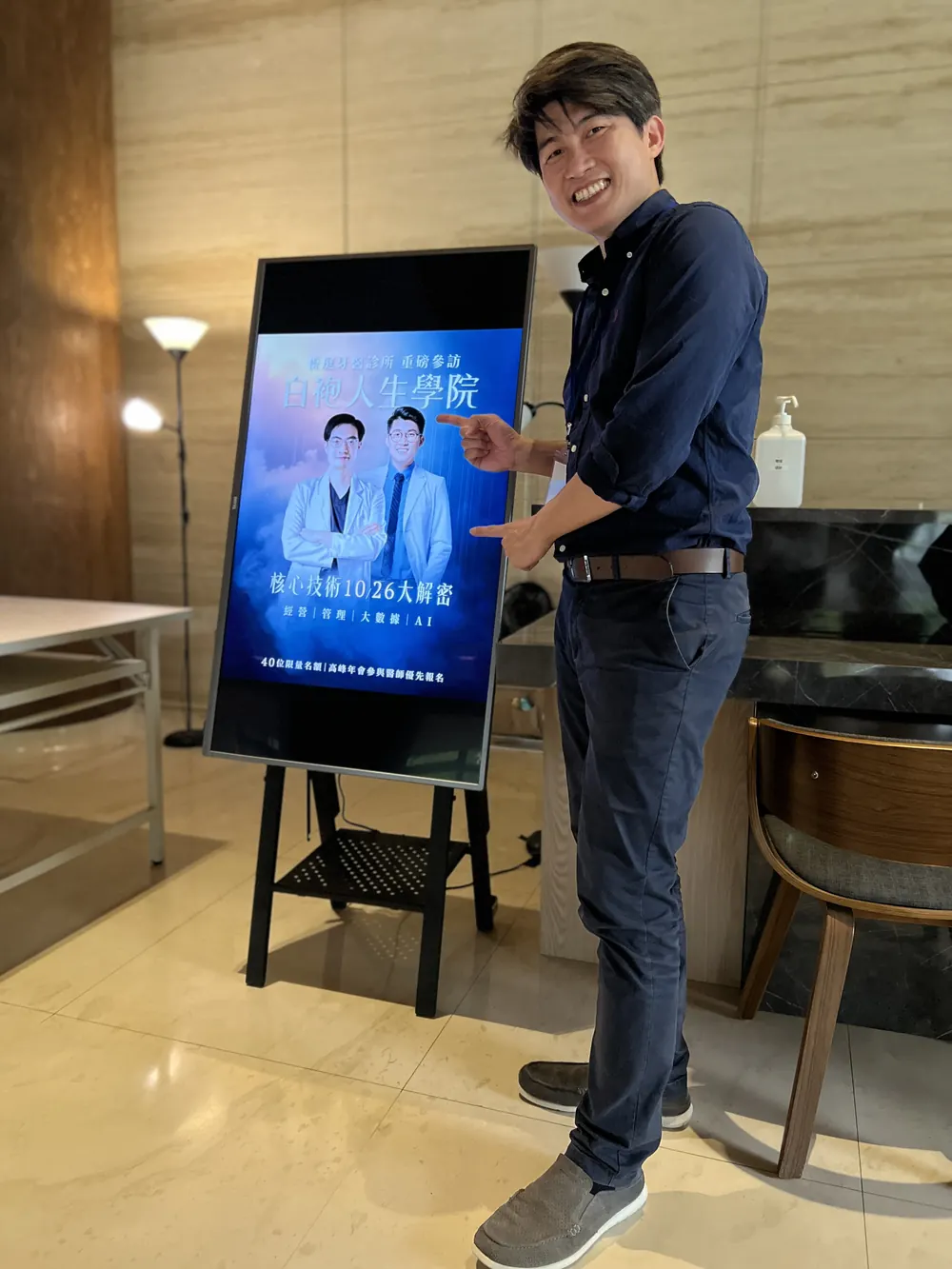 張益豪醫師站在電子立牌旁，指著活動主視覺