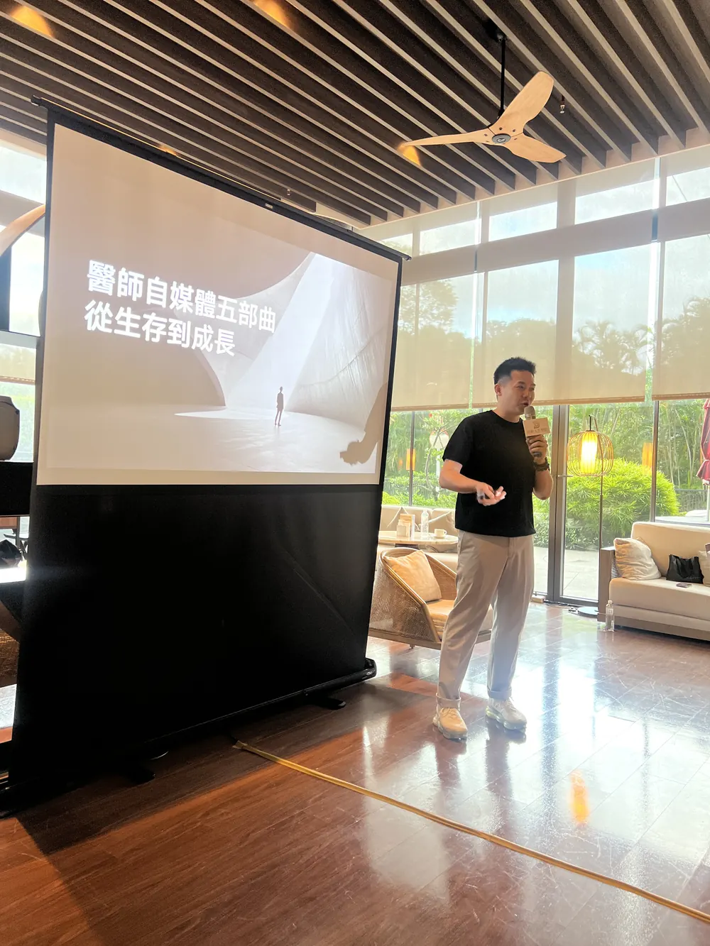 老獅 Lion 站在投影幕旁，投影片寫著「醫師自媒體五部曲 從生存到成長」