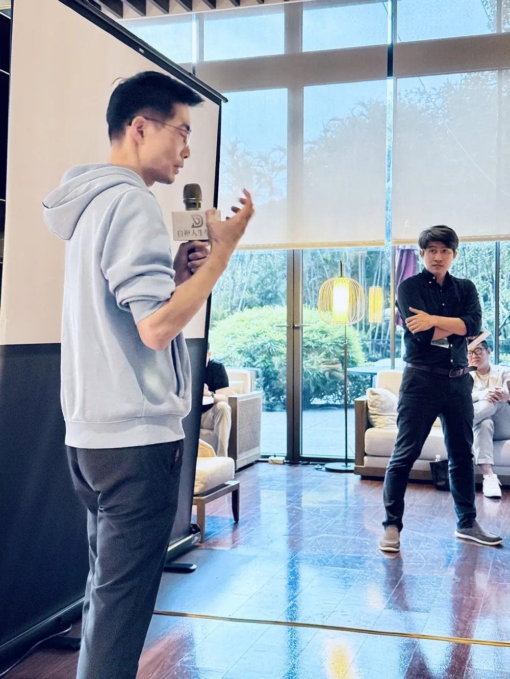 曹皓崴院長手持麥克風說話，張益豪醫師雙手交叉站在後方