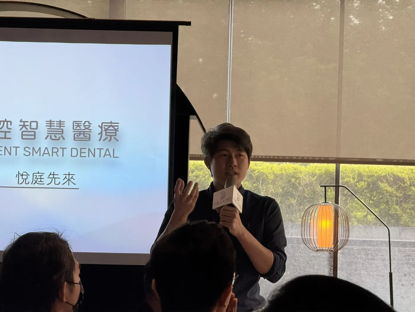 一位與會者站在「悅庭口腔智慧醫療」投影片旁手持麥克風發言