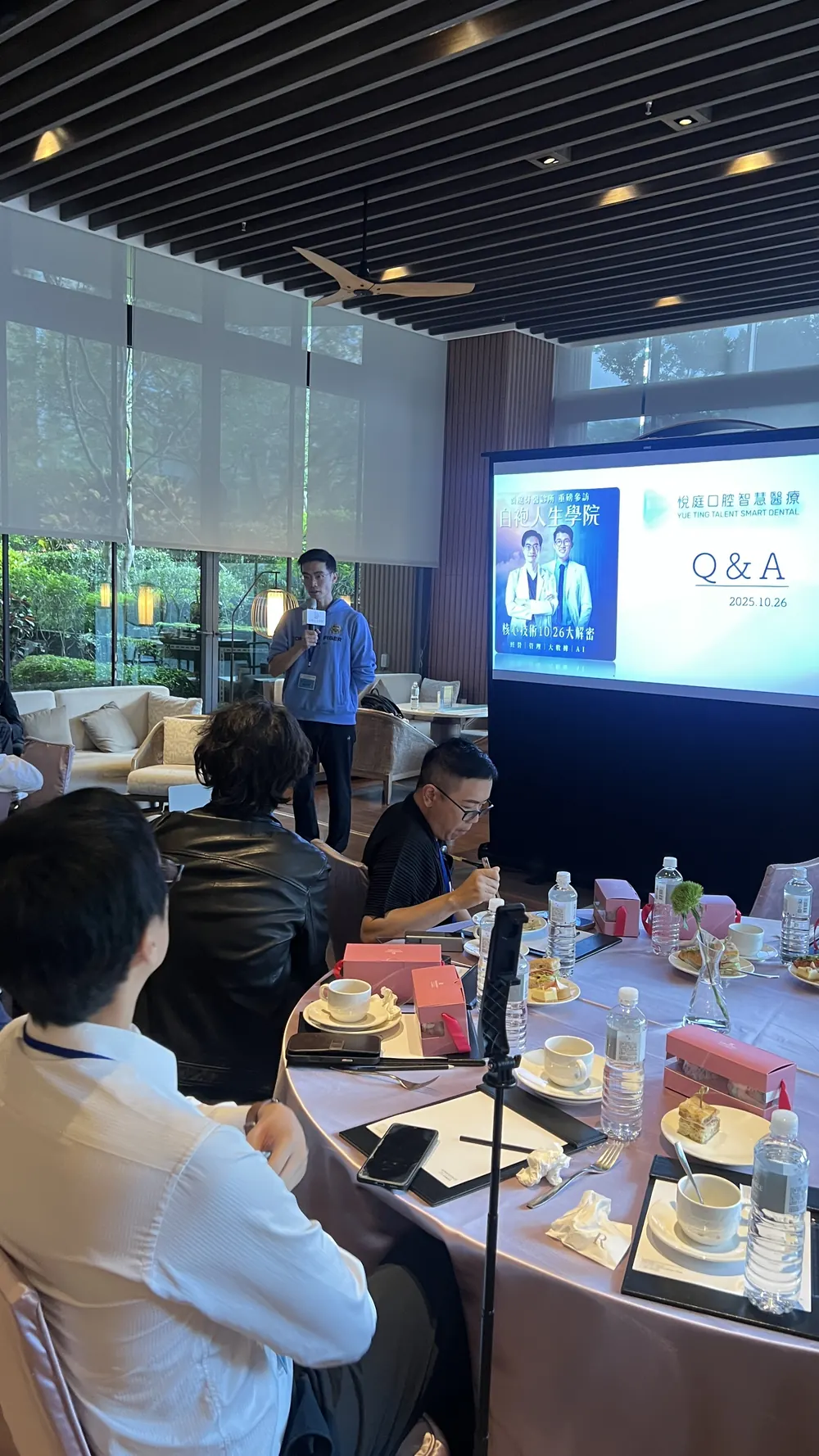 一位與會者手持麥克風站在 Q&A 投影片旁，台下醫師回頭聆聽