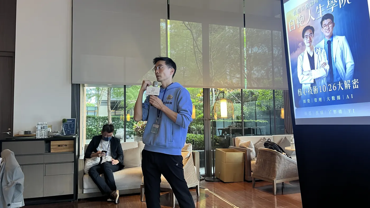 曹皓崴院長手持麥克風，站在白袍人生學院活動主視覺螢幕旁回答問題