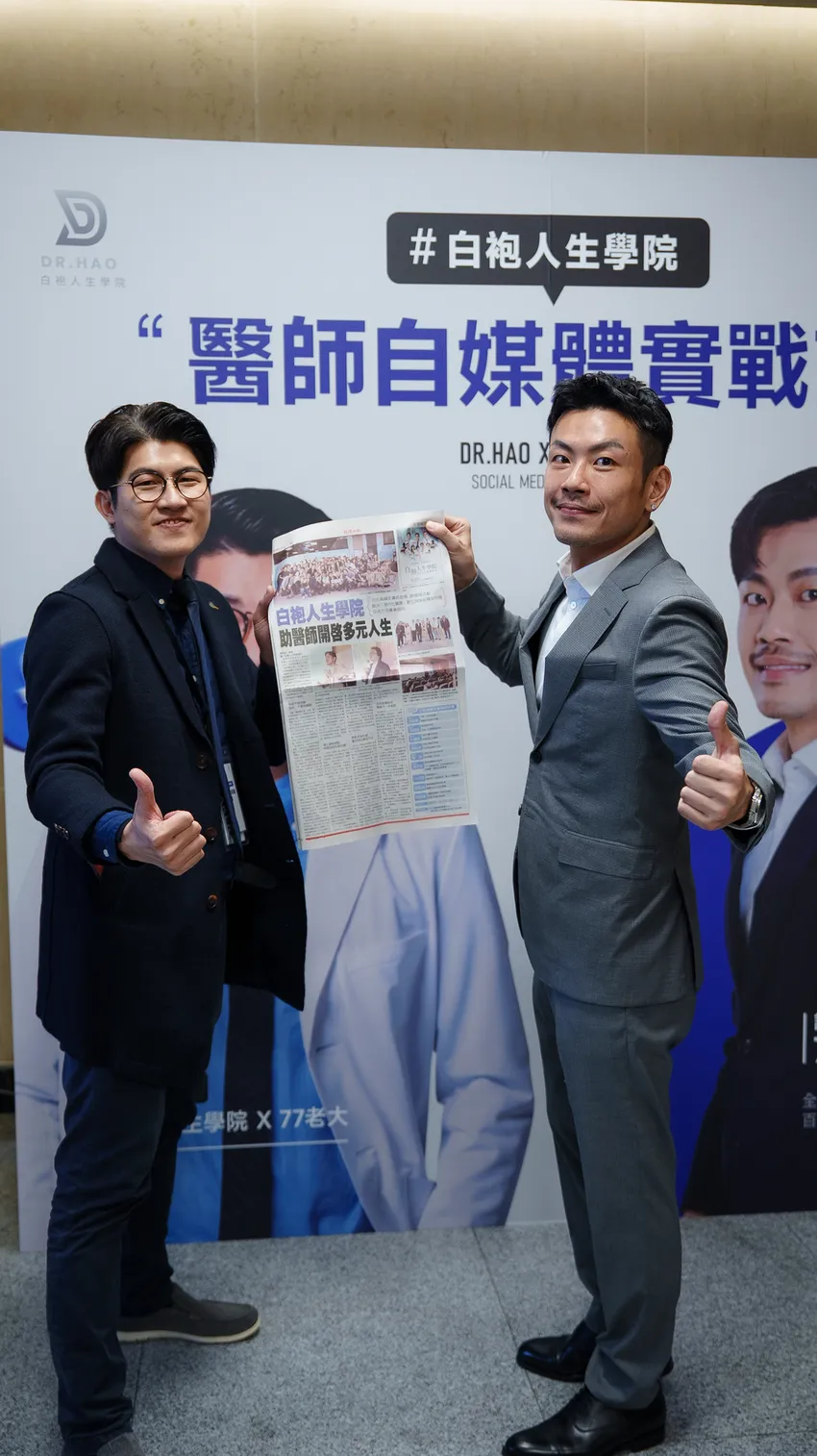 張益豪醫師與 77 老大在活動背板前合影，手持刊有白袍人生學院報導的經濟日報