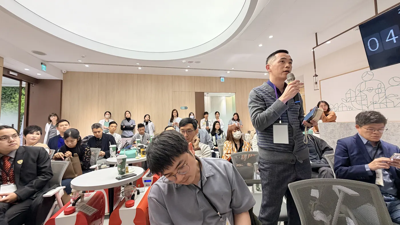 與會醫師站在座位間手持麥克風發言，其他人轉頭聆聽