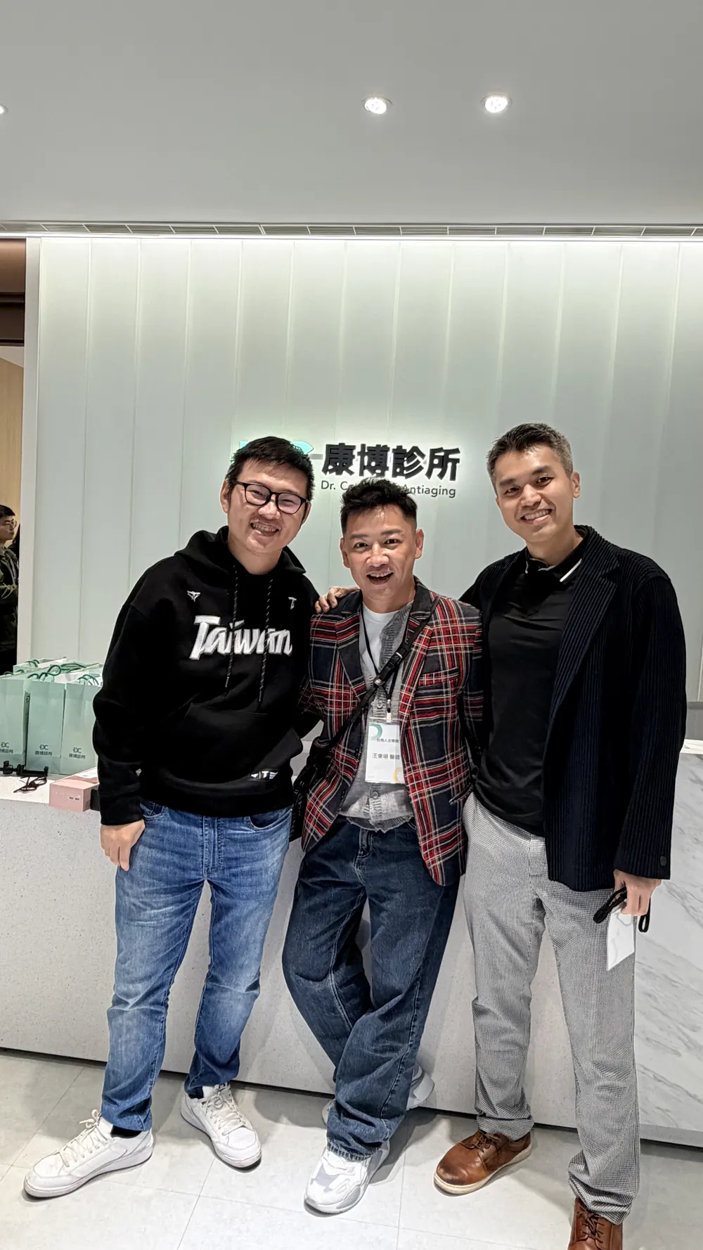 林建佑醫師、王東明老師與陳彥宏醫師在康博診所招牌前合影，近一點