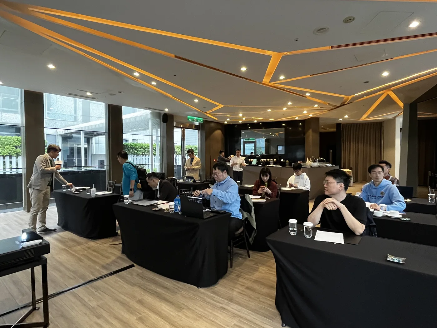 QUUBE 廳會場全景，長桌與投影幕，與會者陸續就座