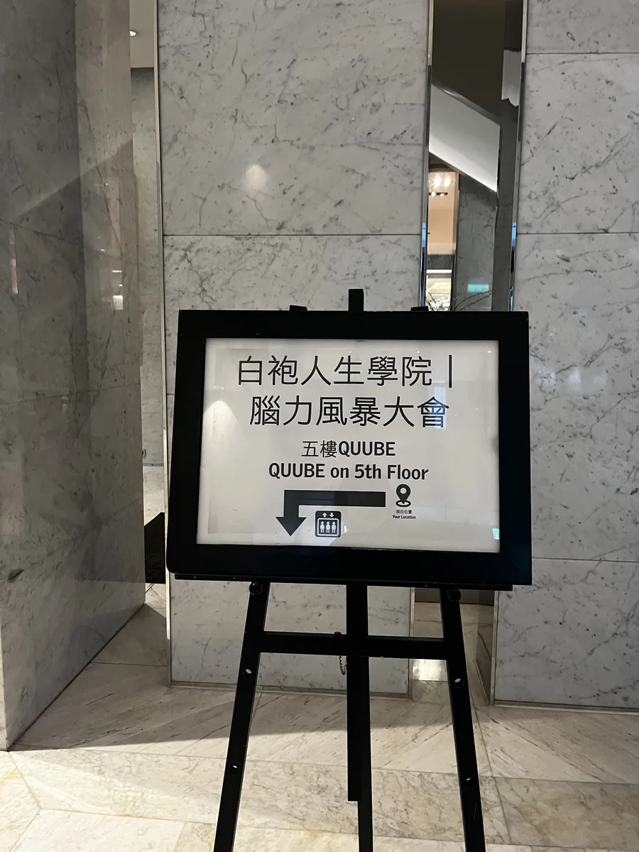 酒店大廳的立牌，寫著白袍人生學院腦力風暴大會五樓 QUUBE