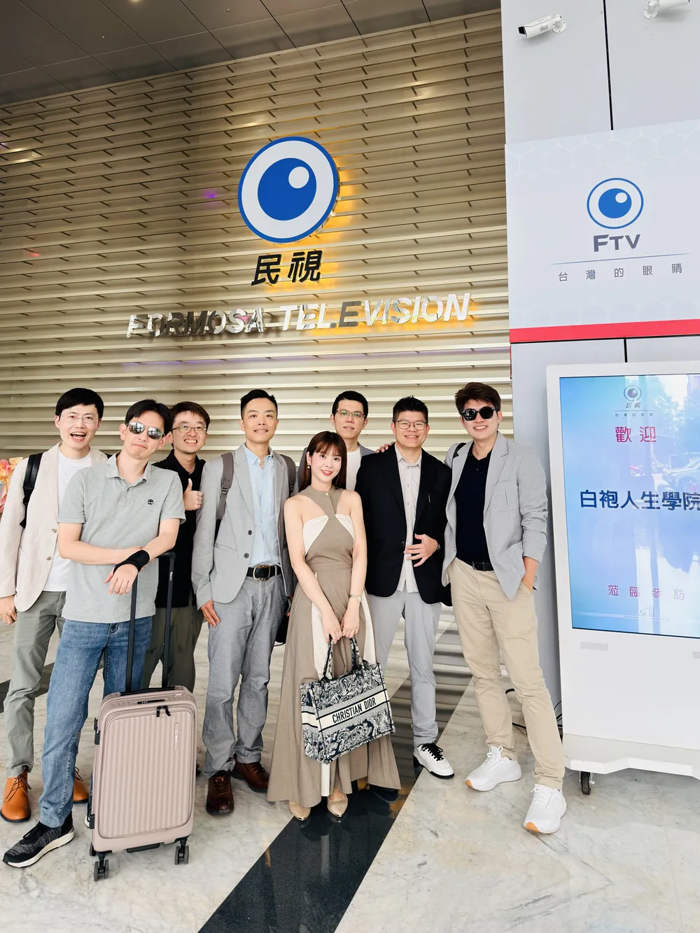 張益豪醫師與先到的醫師在民視大廳的民視標誌牆與歡迎立牌前合影