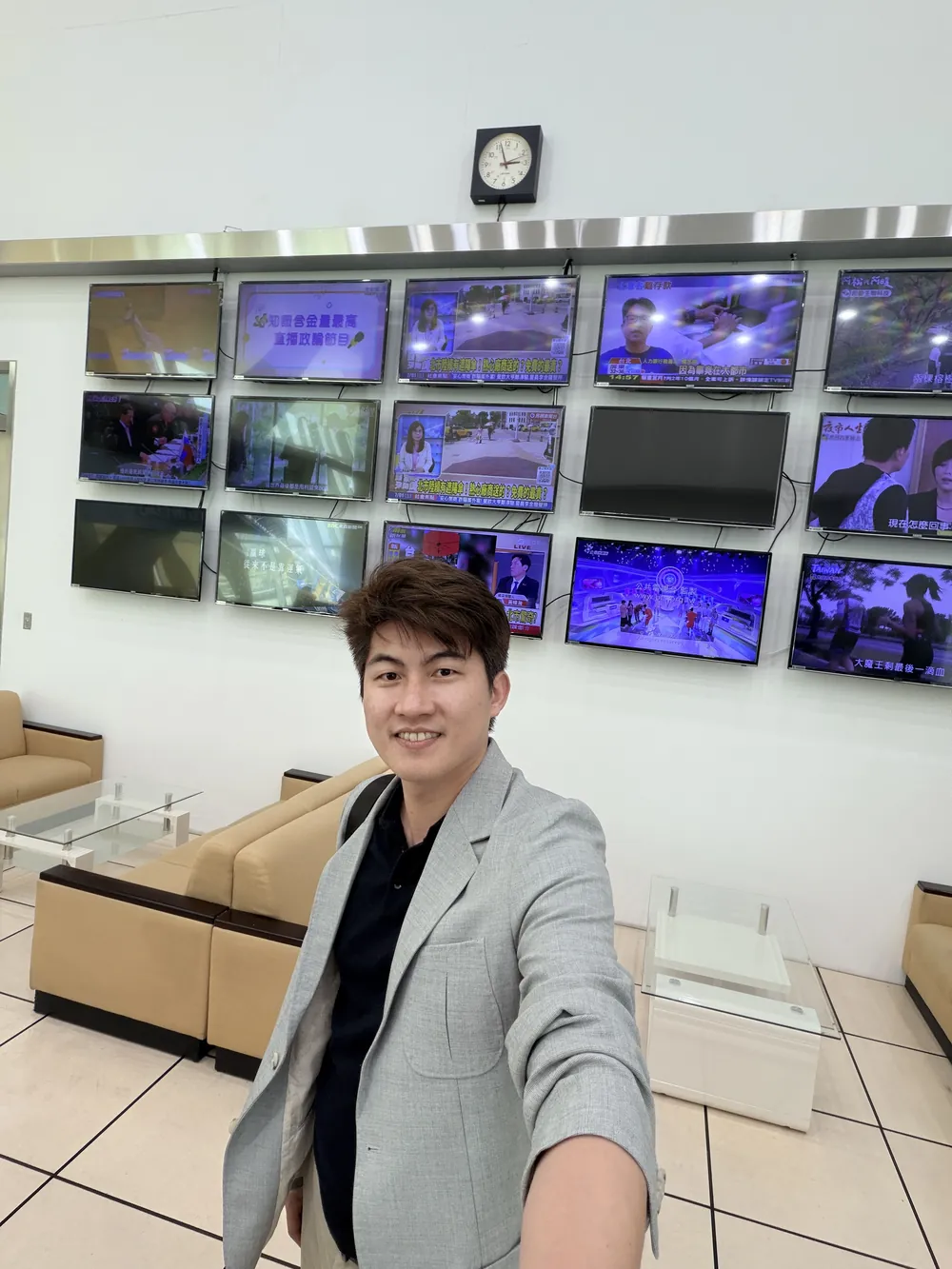 張益豪醫師在一整面電視牆前自拍，牆上同時播放多個新聞頻道
